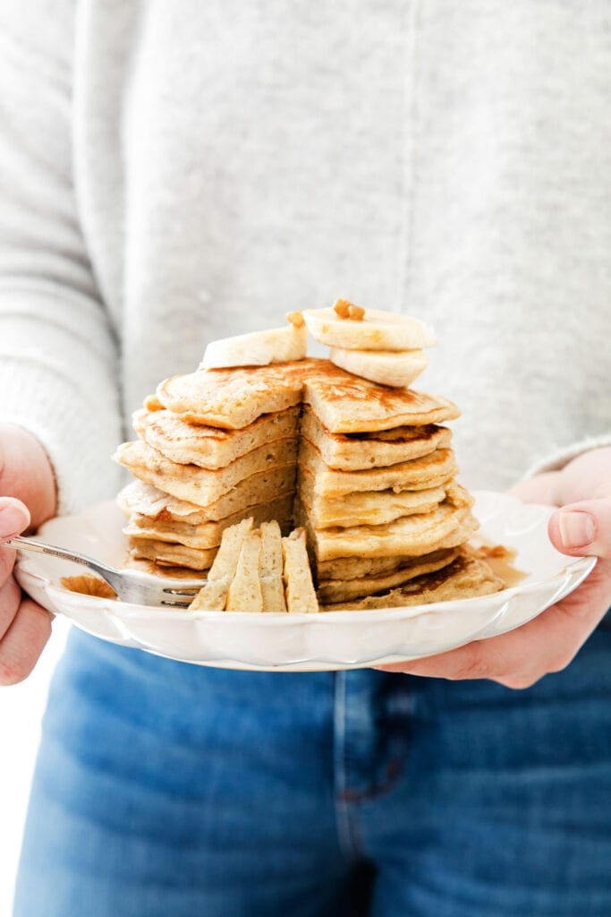 håller en tallrik med lätta bananpannkakor.