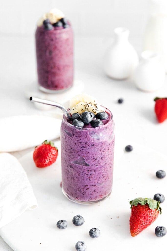 triple berry smoothie in a glass topped with fresh blueberries.