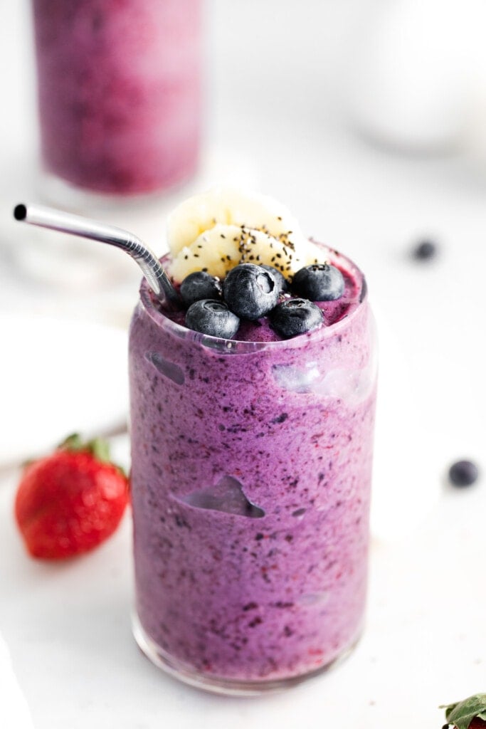 triple berry smoothie in a glass topped with fresh blueberries.