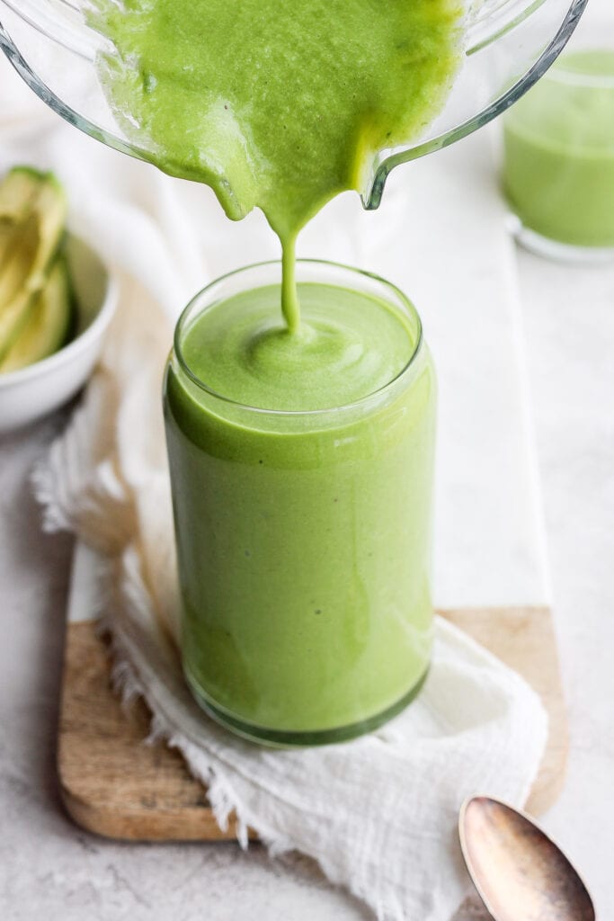 avocado smoothie being poured from a blender to a glass