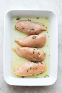 chicken breasts in a white dish with herbs.