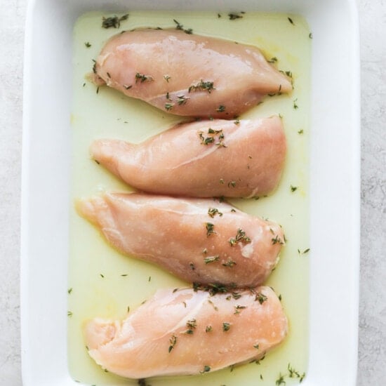 chicken breasts in a white dish with herbs.