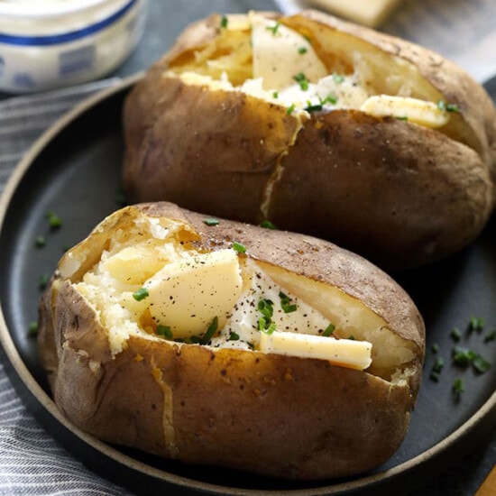 two baked potatoes with cheese on a plate.