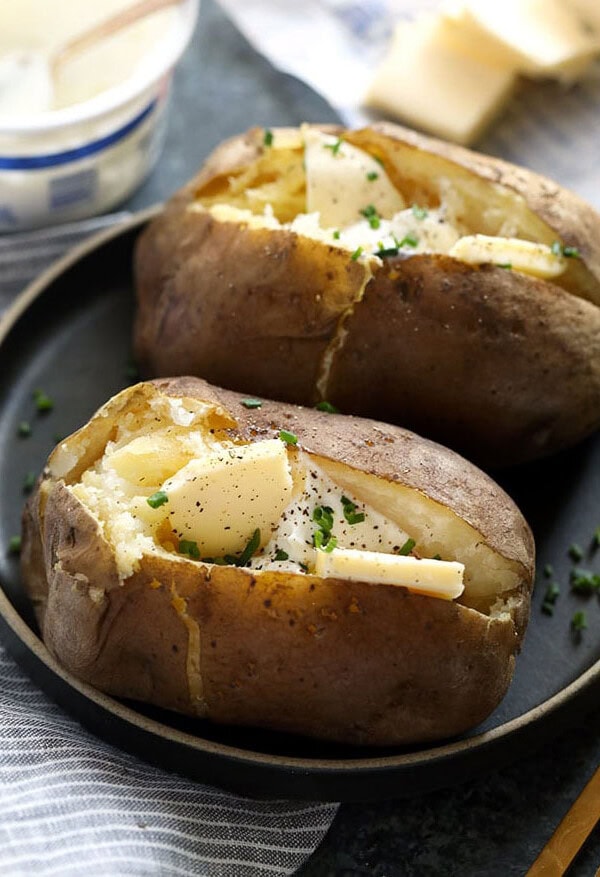 two baked potatoes with cheese on a plate.