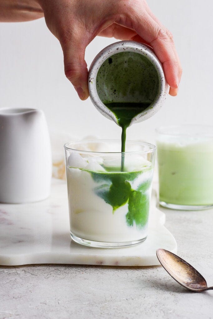 Pouring matcha mixture into the almond milk. 