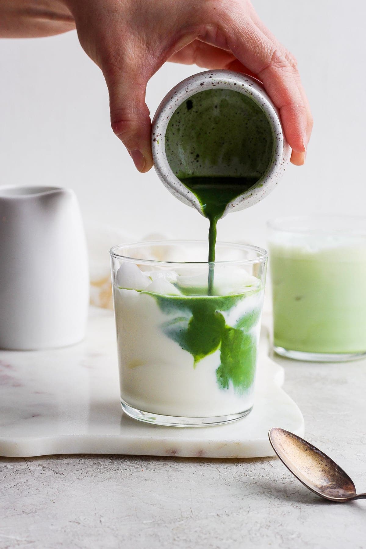 Pouring matcha mixture into the almond milk. 