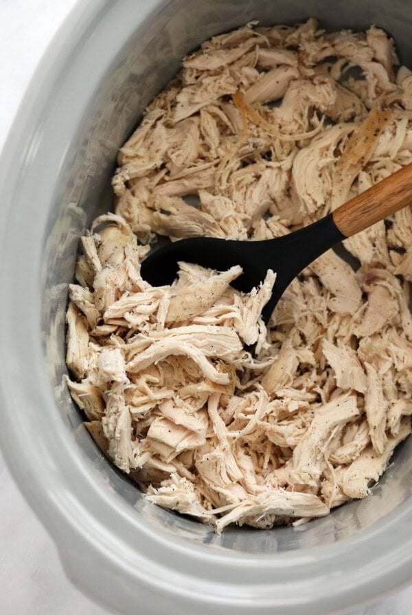 Slow cooker chicken with wooden spoon.