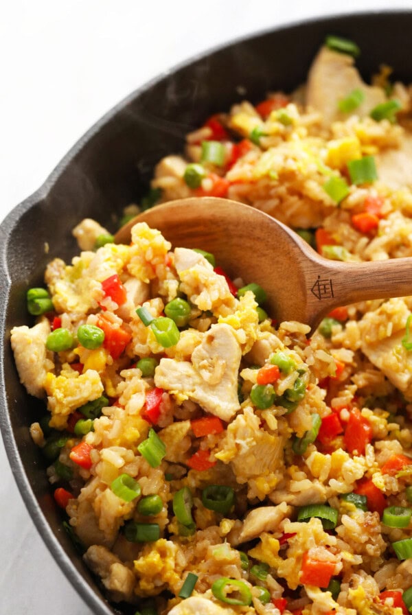 chicken fried rice in a skillet with a wooden spoon.