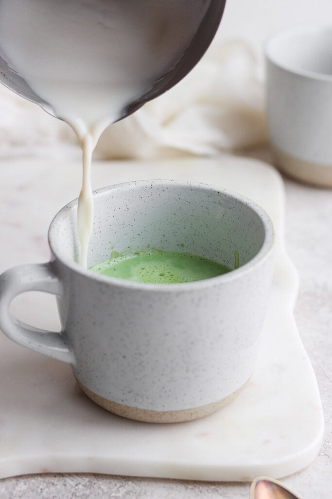 pouring steamed milk on top of matcha powder in mug
