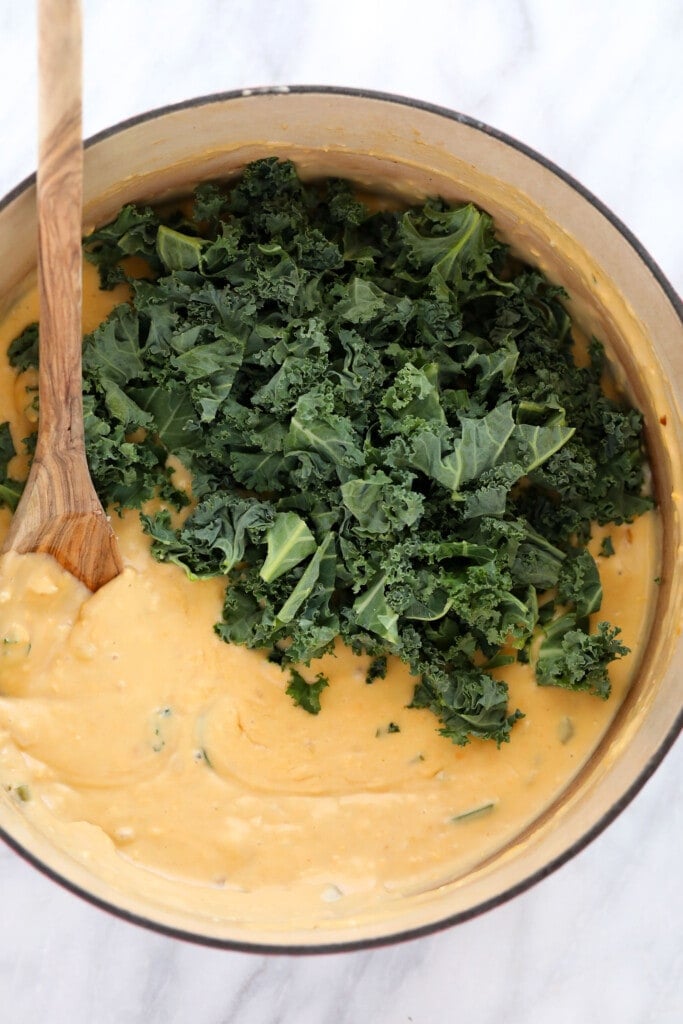 cheese sauce with fresh kale added in, ready to be mixed together for quinoa mac and cheese