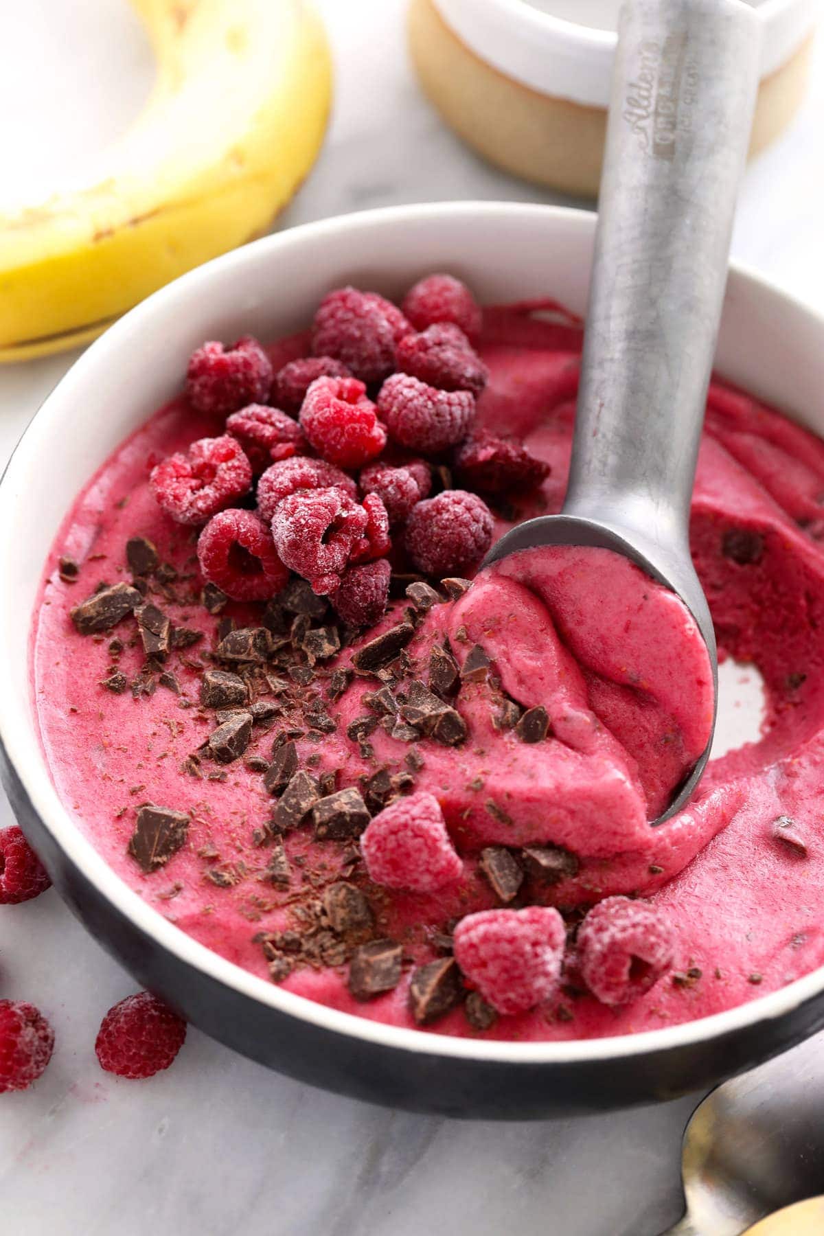 raspberry chocolate chunk banana nice cream in a bowl being scooped with an ice cream scooper