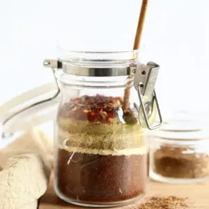 A homemade taco seasoning mix in a glass jar with a wooden spoon.