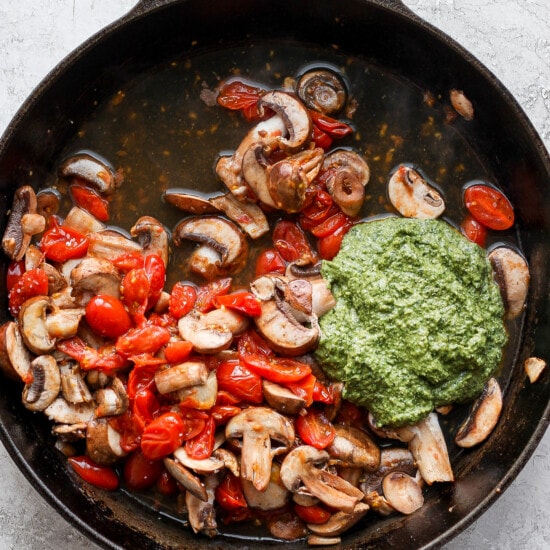 mushrooms and tomatoes in a skillet with pesto sauce.