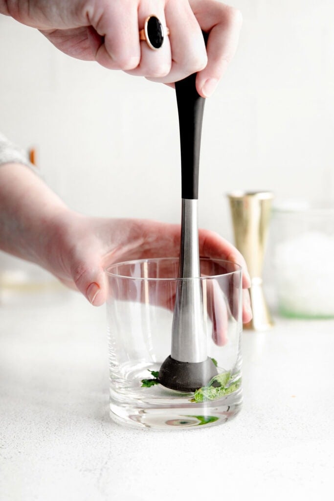 mint being muddled in the bottom of a glass for mint juleps.