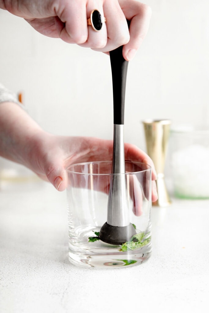 mint being muddled in the bottom of a glass for mint juleps.