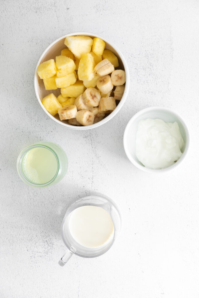 pineapple, banana, Greek yogurt, pineapple juice, and almond milk on countertop