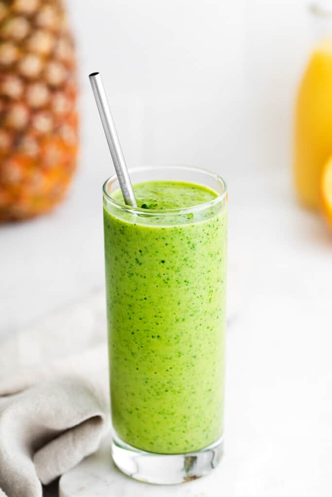 A tropical spinach smoothie in a tall glass with a straw. 