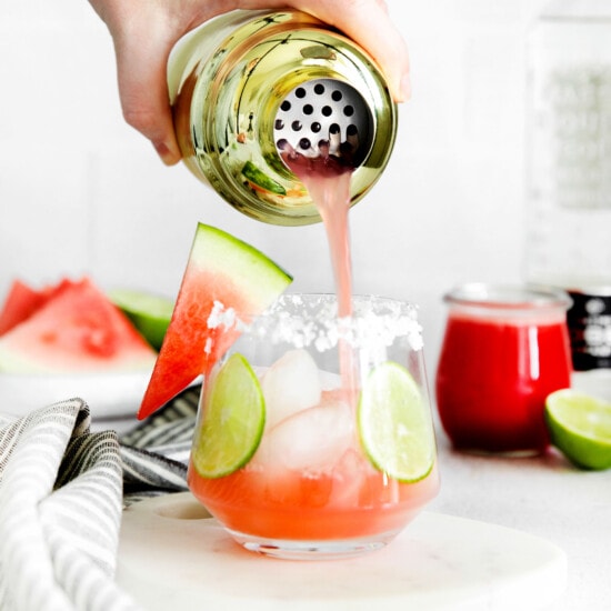 a person pouring watermelon into a margarita glass.