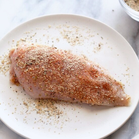 A piece of chicken on a plate with spices on it.