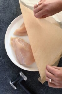 A person slicing a piece of chicken on a plate.