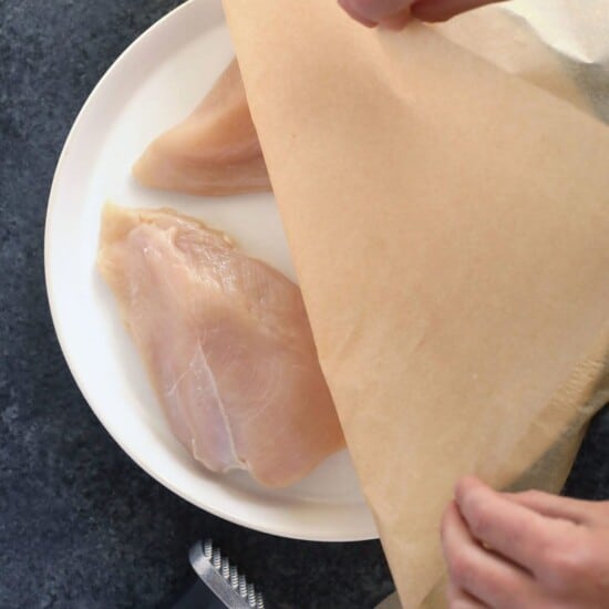 A person slicing a piece of chicken on a plate.