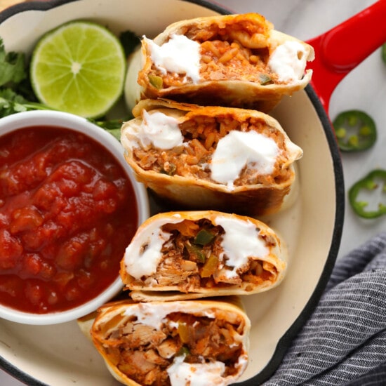 mexican chicken burritos on a plate with sour cream and salsa.