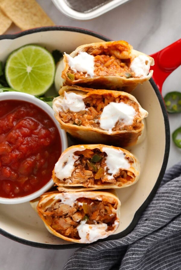 mexican chicken burritos on a plate with sour cream and salsa.