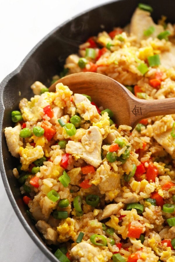 chicken fried rice in a skillet with a wooden spoon.