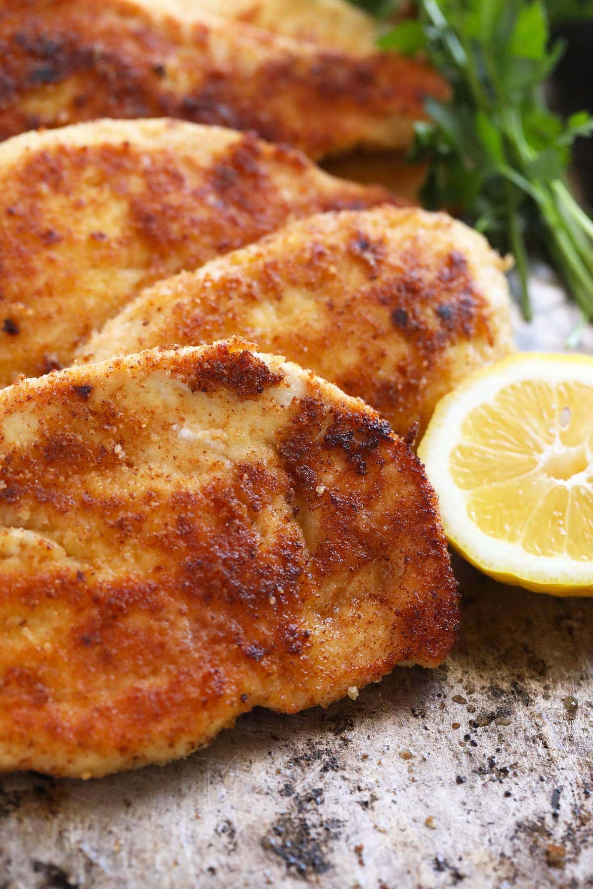 crispy parmesan crusted chicken breast next to lemon wedge