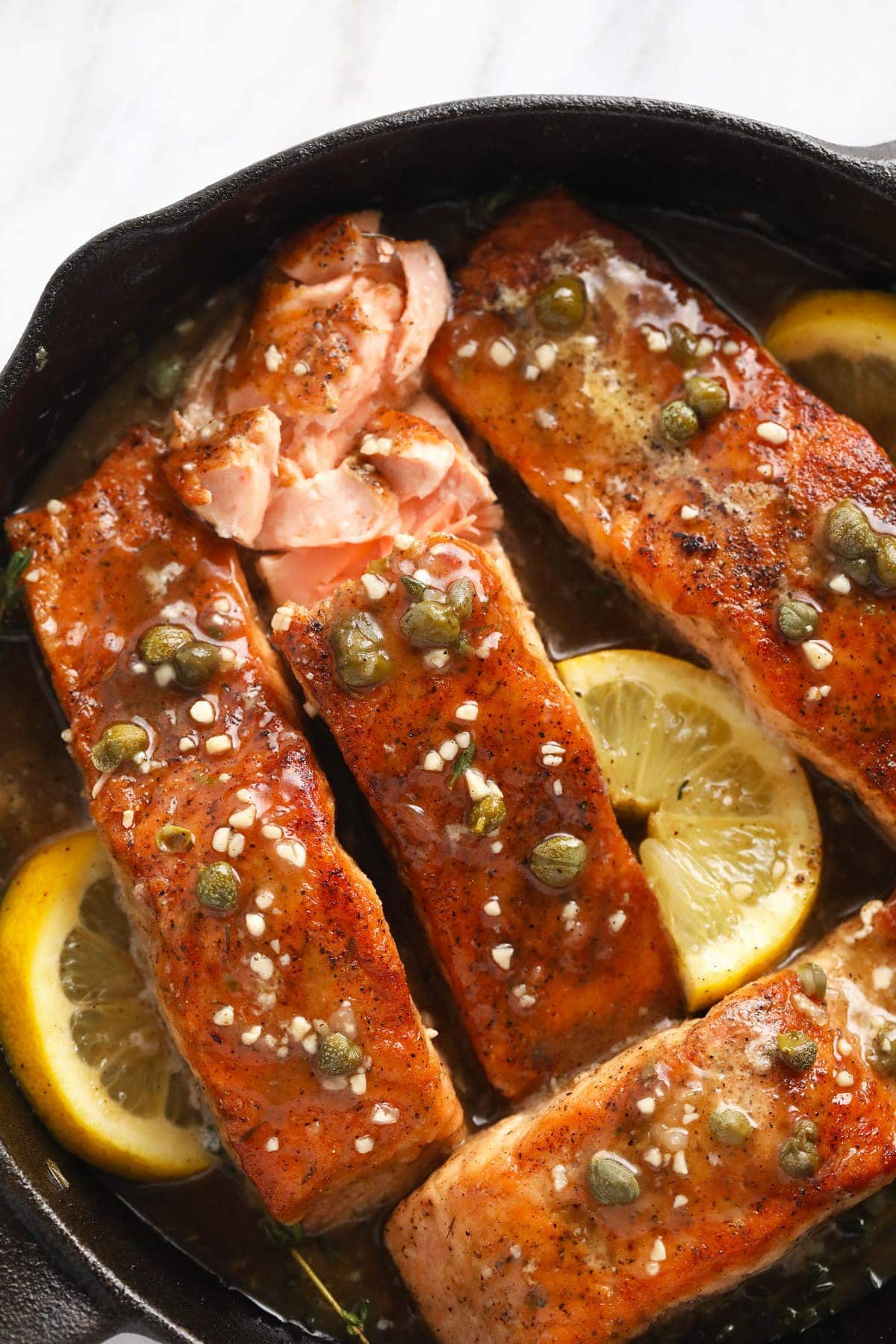 Salmon piccata in a cast iron pan with lemons, capers, and garlic. 