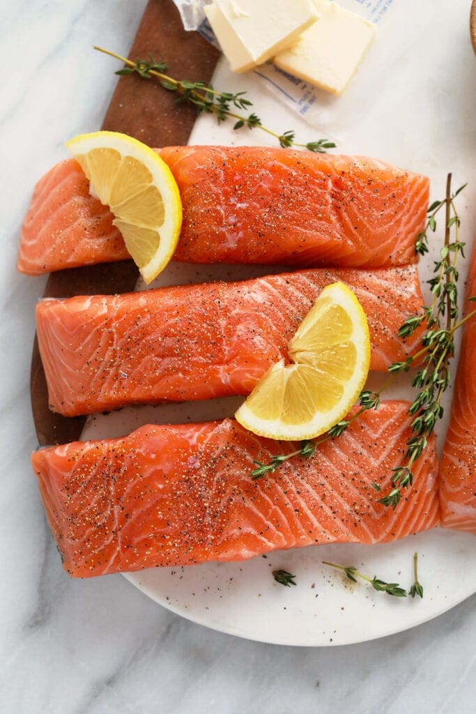 Raw salmon with salt, pepper, fresh lemon, and thyme on a plate. 