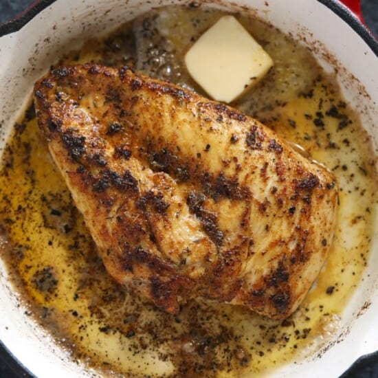 A frying pan with a piece of chicken in it.