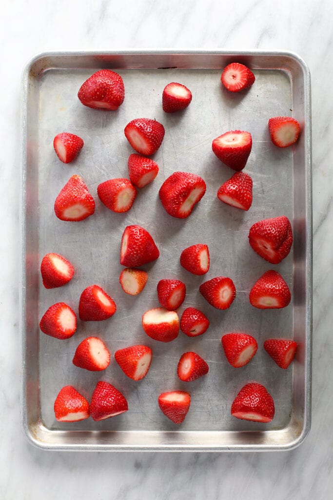 Strawberries spread out on a baking sheet. 