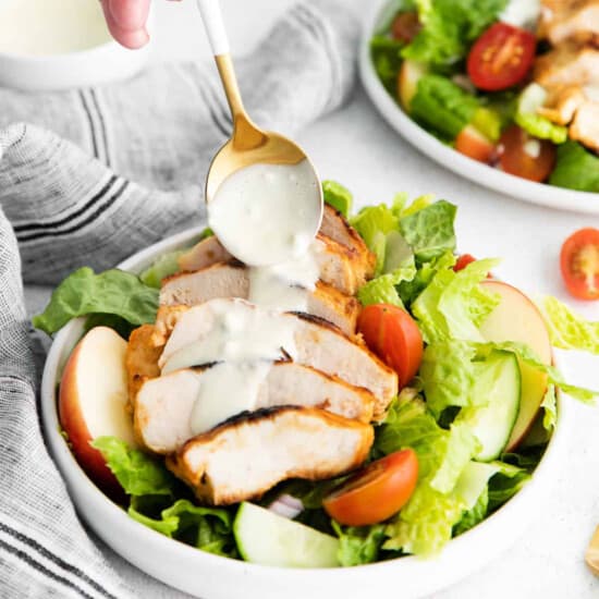 a person drizzling a dressing on a chicken salad.
