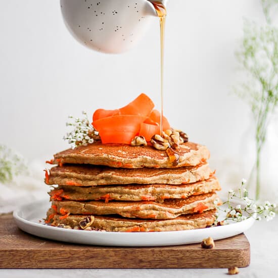 a stack of carrot pancakes being drizzled with syrup.