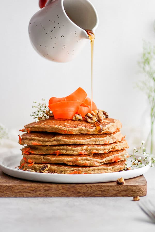 a stack of carrot pancakes being drizzled with syrup.