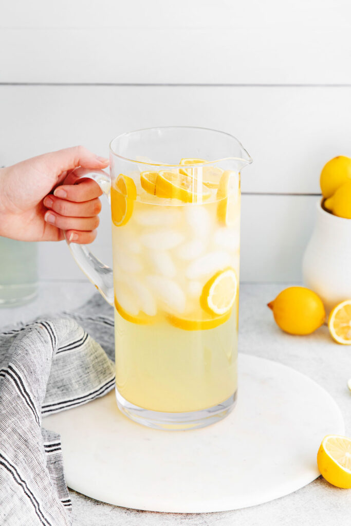 A pitcher of lemonade with ice and slices of lemons. 