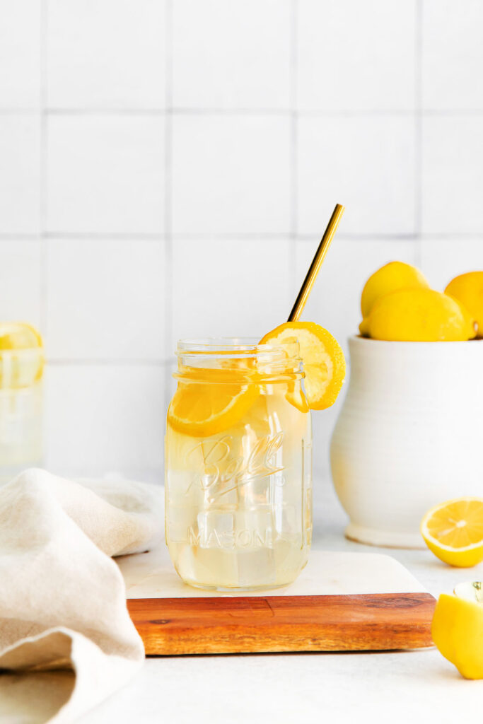 A jar of lemonade with a straw and lemon slices. 