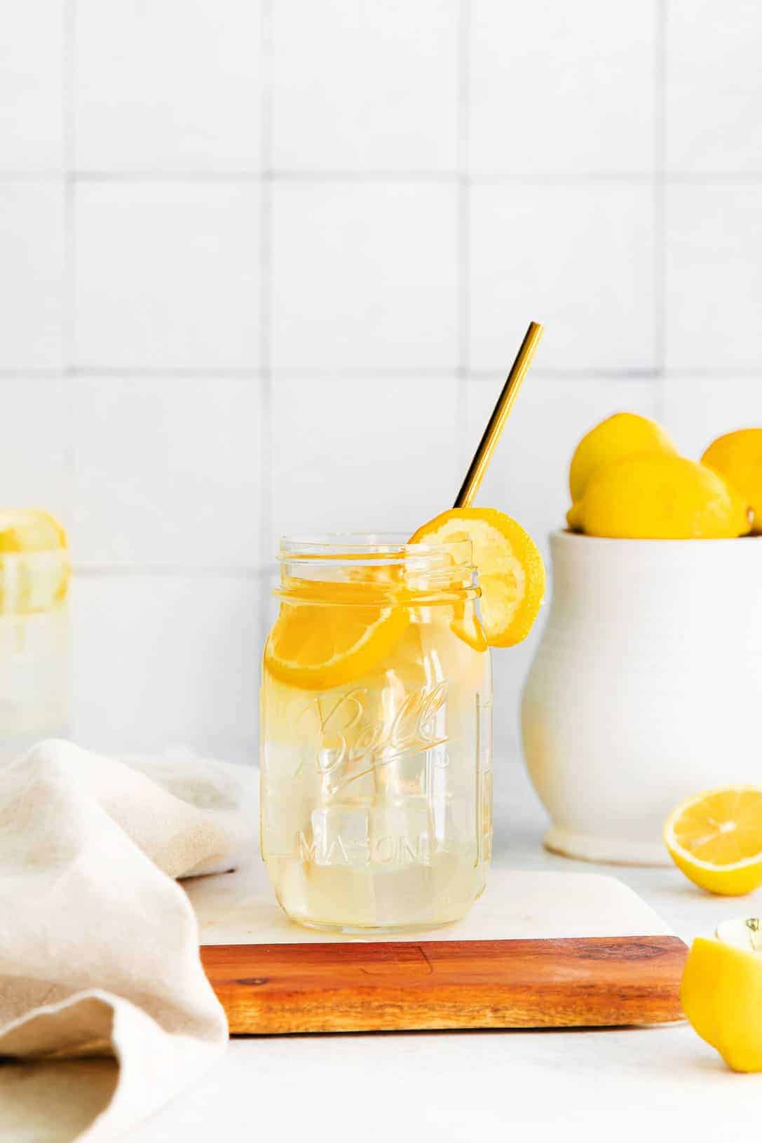 A jar of lemonade with a straw and lemon slices. 