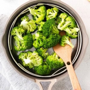 a person is slicing broccoli in a pan with a wooden spoon.