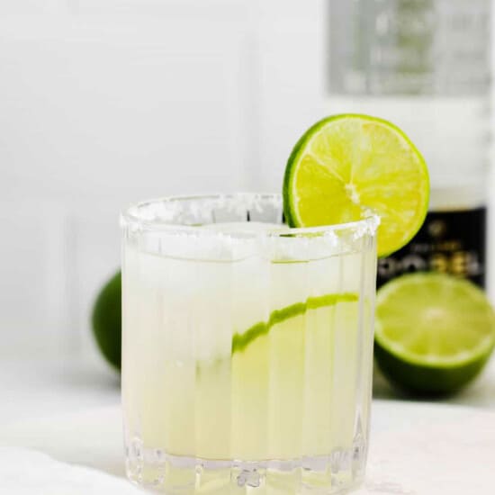 a margarita glass with a lime wedge and a bottle of tequila.