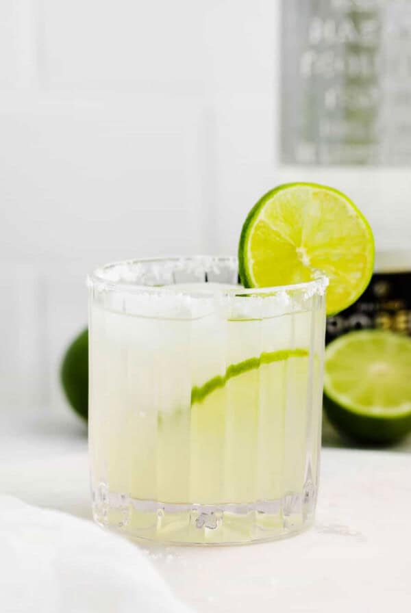 a margarita glass with a lime wedge and a bottle of tequila.