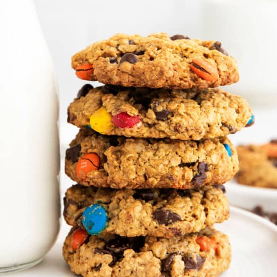a stack of oatmeal m&m cookies next to a glass of milk.
