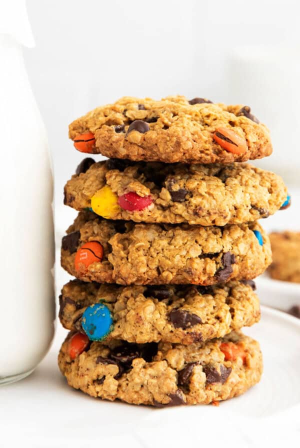 a stack of oatmeal m&m cookies next to a glass of milk.