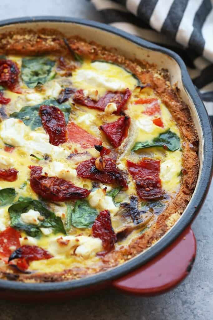 a quiche with spinach and tomatoes in a cast iron pan.