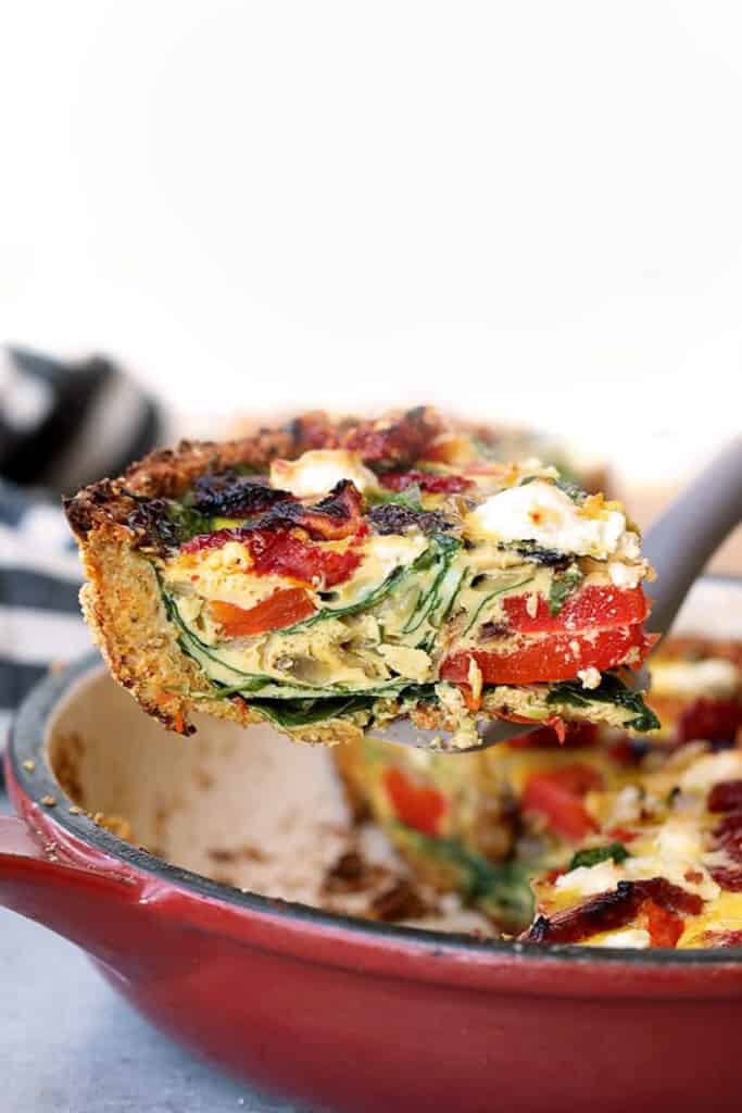 a slice of spinach and bacon quiche in a red skillet.