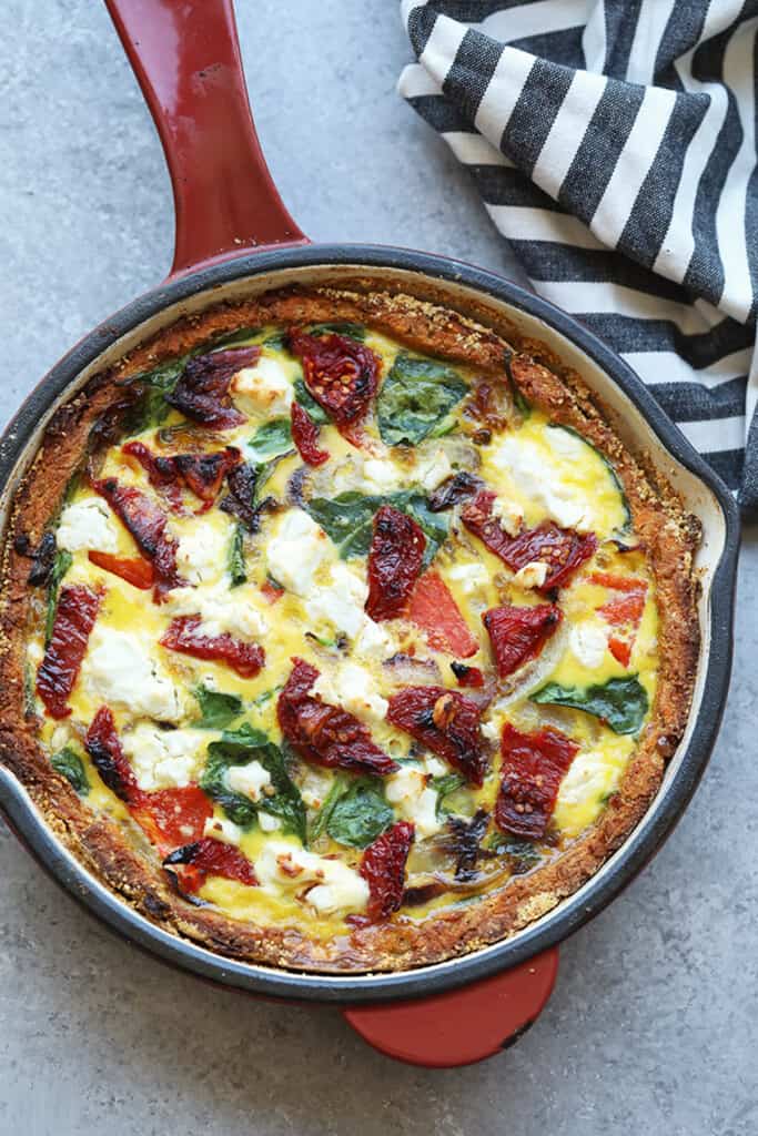 a quiche with spinach and tomatoes in a skillet.