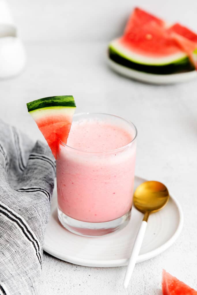 A watermelon smoothie in a glass that is garnished with a fresh chunk of watermelon. 