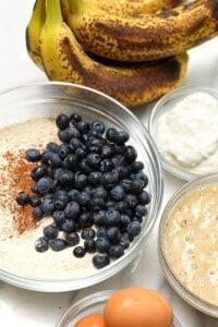 A table topped with bowls of food and bananas, including blueberry banana bread.