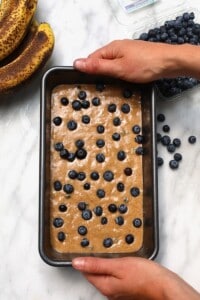 A person holding a pan of blueberry banana bread.